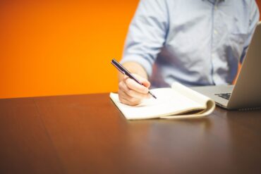 Un homme, entrepreneur est assis et écrit avec un stylo noir sur un block note.
