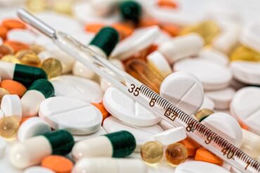 Un thermomètre posé au milieu de pilules de toutes les couleurs.